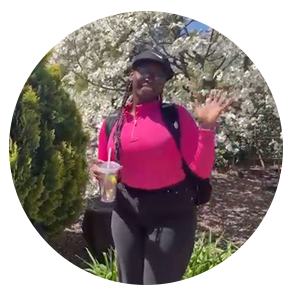 Nyasha stands in front of a flowering tree and waves happily at the camera